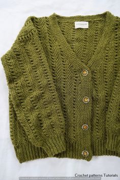 a green knitted sweater with buttons on the front and back, sitting on top of a white sheet