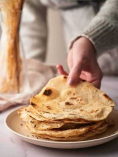 a stack of flatbreads on a plate with a person reaching for one bread