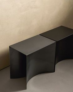 two black tables sitting next to each other on a floor in front of a wall