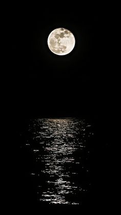 the full moon is reflected in the water on a dark night with only one light visible