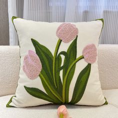 a pillow with pink flowers on it sitting on a couch next to a flower vase