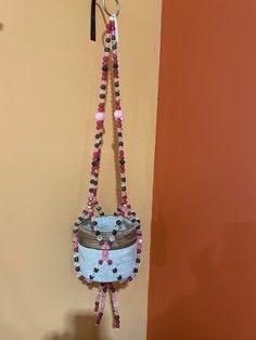 a small purse hanging from a hook on a wall with beads and chains attached to it