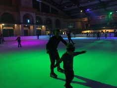 people skating on an ice rink at night with green lights and blue sky in the background