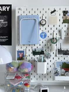 a white desk topped with lots of clutter next to a wall mounted calendar and cell phone