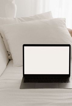 an open laptop computer sitting on top of a white bed covered in pillows and blankets