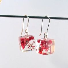 the earrings are made from glass and have red flowers in them, hanging on a wire