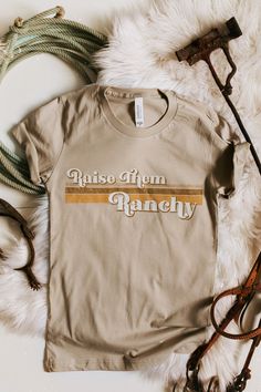 "✨ Raise Them Ranchy ✨ This shirt is high quality and super comfy! All you ranch mama's need this shirt! Tag us on Instagram @wildthreadsandco of you wearing our Raise them Ranchy shirt!   Please allow 2-3 days for printing 🌵CARE INSTRUCTIONS 🌵 For the longest lifespan for your Wild Threads + Co. shirt, we recommend turning your tee inside out, washing with cool water and hanging them to dry. We advise you to not use bleach. ⚡️ SIZING ⚡️ Measurements are from armpit to armpit and length is fro Country Style Crew Neck Top With Graphic Print, Country Style Pre-shrunk Cotton T-shirt, Country Style Cotton Pre-shrunk T-shirt, Country Style Cotton T-shirt, Relaxed Fit Country Style Crew Neck T-shirt, Country Style Relaxed Fit Cotton T-shirt, Country Style White Cotton T-shirt, Country Style Cotton Tops With Letter Print, Country Style Cotton T-shirt With Short Sleeves