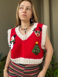 a woman standing in front of a plant wearing a red sweater with christmas decorations on it