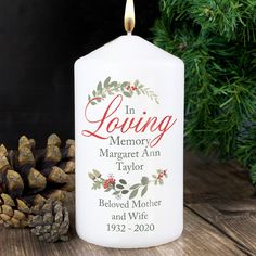 a white candle with the words in loving memory on it and pine cones next to it