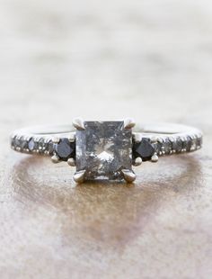 an engagement ring with a square cut diamond surrounded by black diamonds