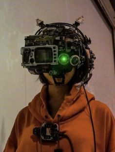 a person wearing an orange hoodie with headpieces made out of electronic equipment