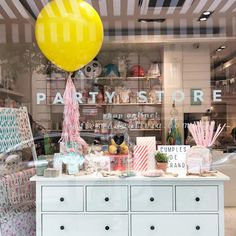 a store window with lots of items on display in front of it and a yellow balloon hanging from the ceiling