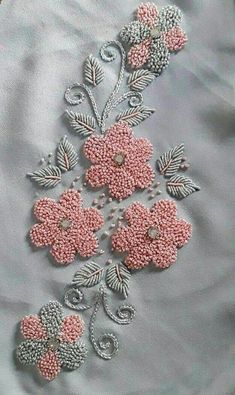 some pink flowers and leaves are on a white cloth with silver thread work in the middle