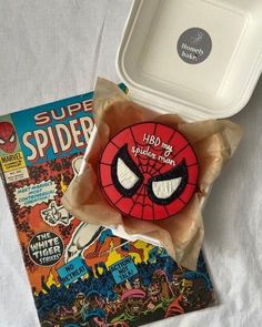 a spider - man pin sitting on top of a book next to a plastic container