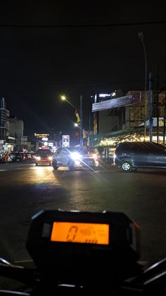 cars are driving down the street at night with traffic lights on and buildings in the background