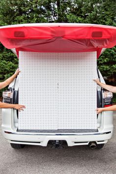 two people standing in front of a white truck with a red surfboard on the back