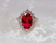 a ring with a large red stone surrounded by small white diamonds on a lace surface