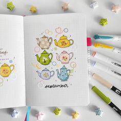 an open notebook with teapots and stars on the pages, surrounded by markers