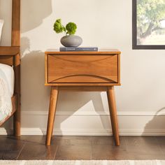 a small wooden table with a potted plant sitting on it's top next to a bed