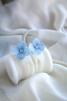 two blue flowers sitting on top of a white cloth next to a beaded necklace