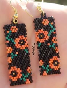 a pair of beaded earrings is shown on someone's hand, with beads in the shape of an orange and black cat