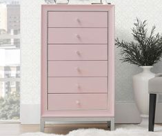 a pink chest of drawers next to a white chair and potted plant in front of a window