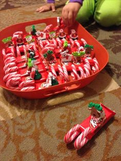 a tray filled with candy canes on top of a floor next to a child