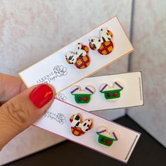 the person is holding two small earrings in front of their earring packagings, which are designed to look like mickey mouse ears