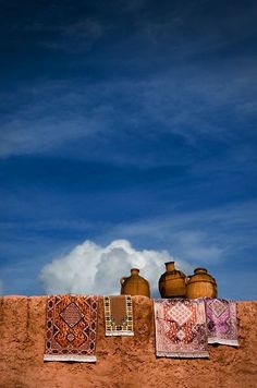 there are vases and rugs hanging on the side of a wall with clouds in the background