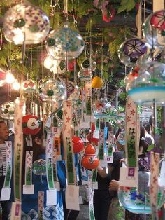 people are looking at christmas ornaments hanging from the ceiling in a market place with lots of them