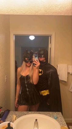 two people dressed as batman and catwoman taking a selfie in a bathroom mirror