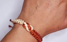 a person's hand with a red and white braided bracelet on their wrist