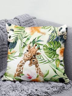 two giraffes on a tropical print pillow sitting on a gray couch next to a white flower