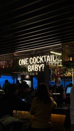 people sitting at tables in a bar with neon signs on the wall above them that read, one cocktail baby?