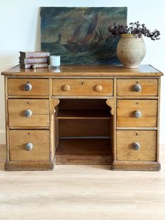 an old wooden desk with drawers and a painting on the wall