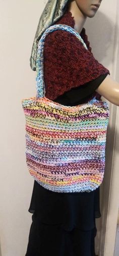 a mannequin is holding a multicolored crocheted bag in front of a white wall