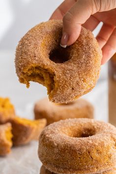 a hand is picking up a sugary doughnut from a stack of other donuts