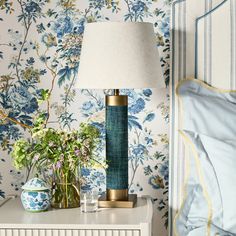 a lamp on a nightstand next to a bed with blue and white wallpapers