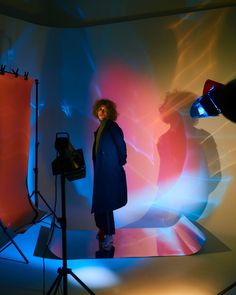 a woman is standing in front of a photo studio with lights on the wall behind her