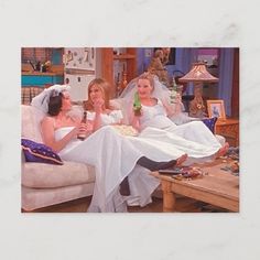 three women in wedding dresses sitting on a couch drinking beer and watching tv with their feet up