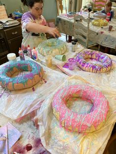 a woman is painting donuts on the table with other items around her and another person in the background