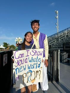 a man and woman standing next to each other holding a sign that says can i show you a whole new world at prom