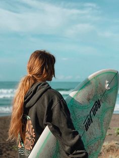 a woman holding a surfboard on top of a sandy beach next to the ocean