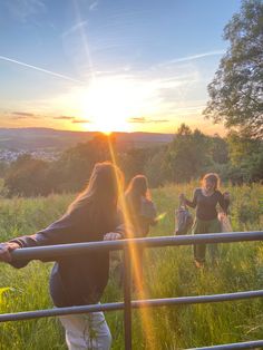 some people are standing in the grass by a fence and watching the sun go down