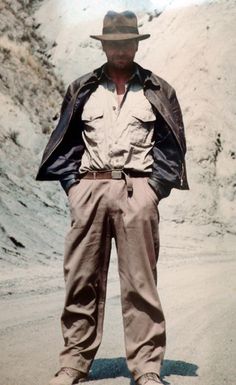 an old photo of a man standing on the side of a road wearing a hat