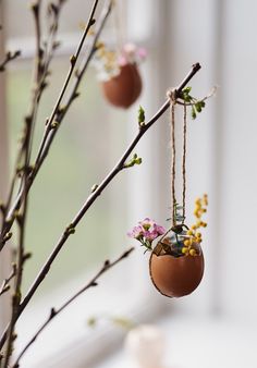 two eggs hanging from branches with flowers in them