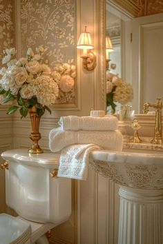 a white sink sitting under a mirror next to a toilet and a vase with flowers