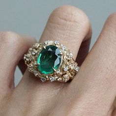 a close up of a person's hand wearing a ring with an oval green stone