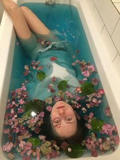 a woman laying down in a bathtub filled with water and flowers on the floor