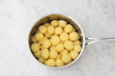 a pot filled with yellow potatoes on top of a white counter next to a spoon